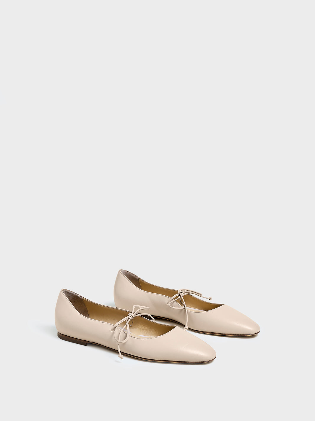 Angle view of a pair of sand leather ballet flats with an almond toe and tie detail.