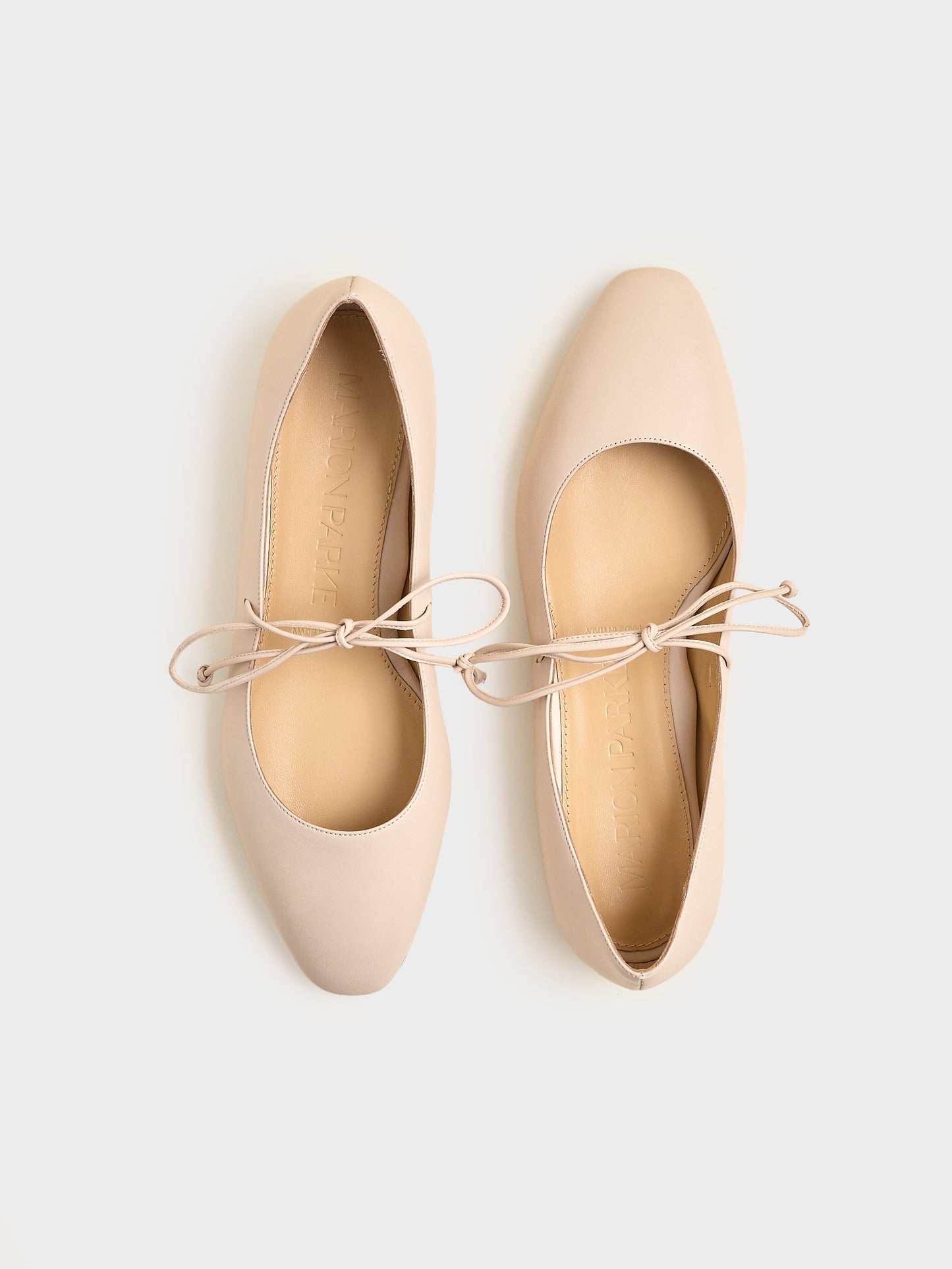 Top view of a pair of sand leather ballet flats with an almond toe and tie detail.