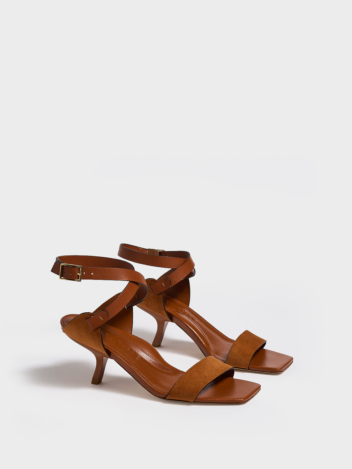 Angle view of a pair of chestnut leather and suede high heel sandals with a sculptural design and adjustable ankle strap. 